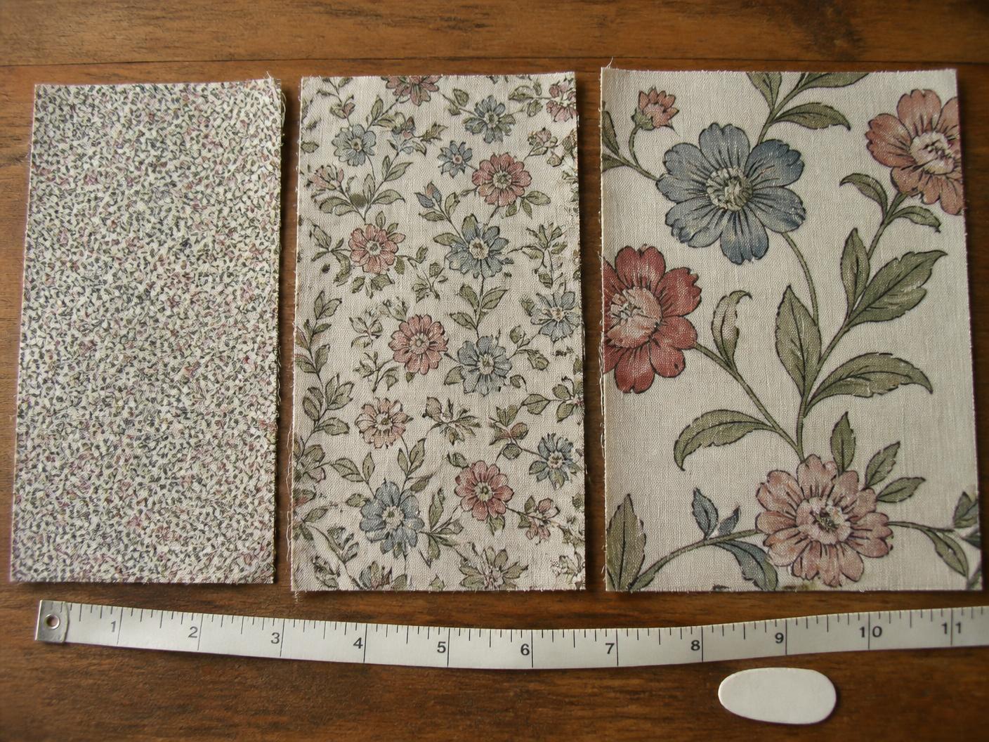 Three printed cotton swatches of the same floral pattern at small, medium and large scale laid side by side beside a measuring tape