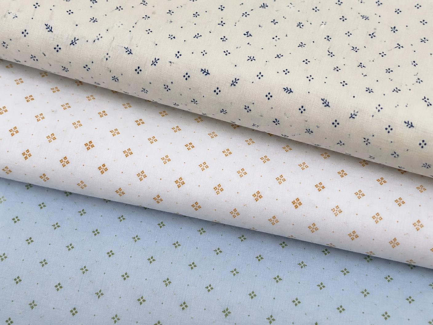 Three folded cotton shirting fabrics printed with tiny ditsy motifs in navy on cream, ochre on white and olive on pale blue